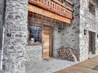 This stunning stone chalet boasts a charming wooden door and balcony, perfect for enjoying mountain views.