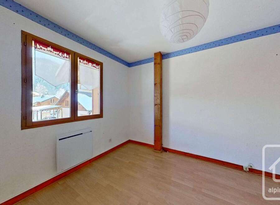 This bright and airy bedroom features a large window offering stunning views of the surrounding mountains.