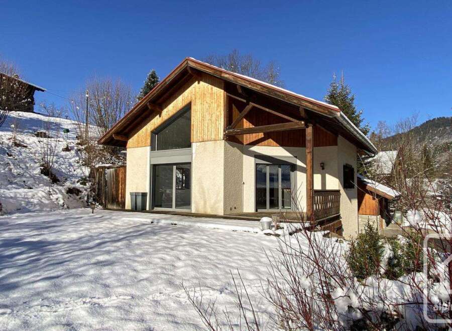 This stunning chalet boasts a modern design with large windows offering breathtaking views, nestled in a picturesque snowy landscape.