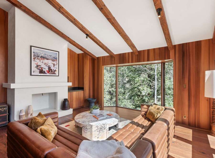 This stunning living room boasts a cozy leather sectional sofa, perfectly positioned to enjoy the expansive window views of the lush forest.
