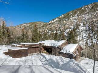 This stunning log cabin nestled in the Colorado mountains boasts a spacious design with a large garage and expansive windows offering breathtaking views.
