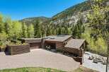 This stunning mountain home boasts a spacious, gravel driveway leading to a rustic-chic log cabin with a modern flat roof extension.