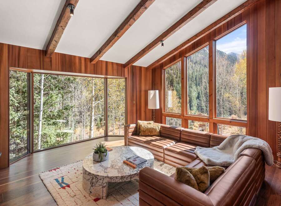 This stunning living room boasts expansive windows showcasing breathtaking mountain views, complemented by rich wood paneling and exposed beams.