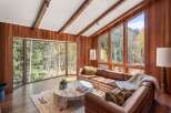 This stunning living room boasts expansive windows showcasing breathtaking mountain views, complemented by rich wood paneling and exposed beams.
