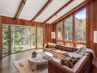 This stunning living room boasts expansive windows showcasing breathtaking mountain views, complemented by rich wood paneling and exposed beams.