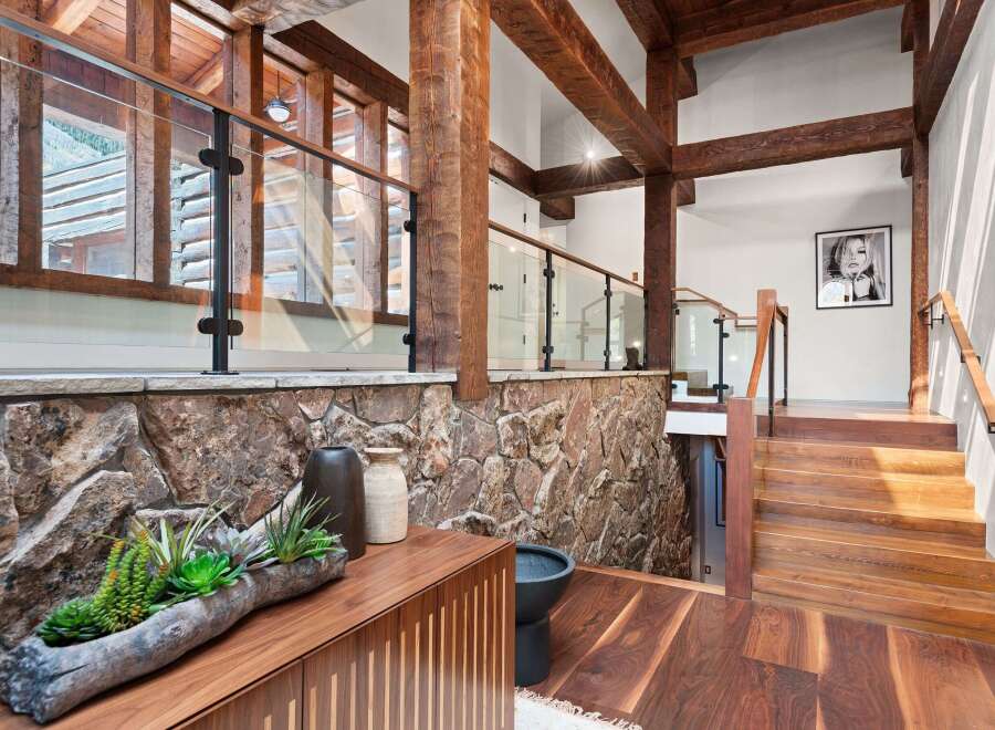 This stunning home boasts a grand entrance with a striking combination of natural wood beams, a rustic stone wall, and a sleek glass railing.