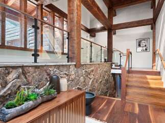 This stunning home boasts a grand entrance with a striking combination of natural wood beams, a rustic stone wall, and a sleek glass railing.