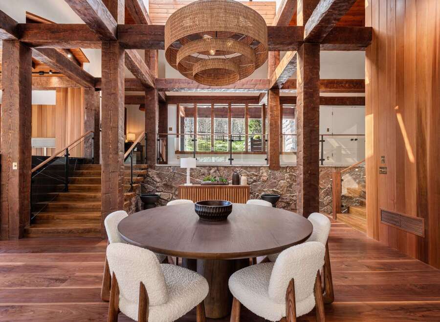 This stunning home boasts a spacious dining area with a large, round wooden table surrounded by cozy white chairs, creating a warm and inviting atmosphere.