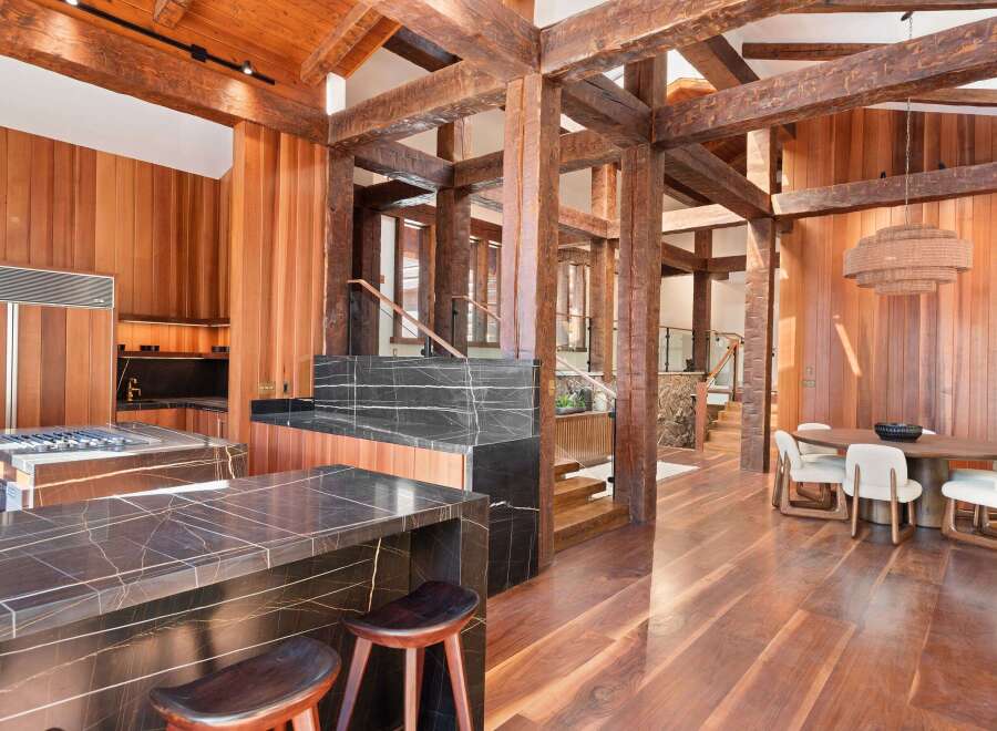 This stunning home boasts a gourmet kitchen with dark marble countertops and high-end appliances, seamlessly flowing into a spacious dining area with a wooden table and plush chairs.