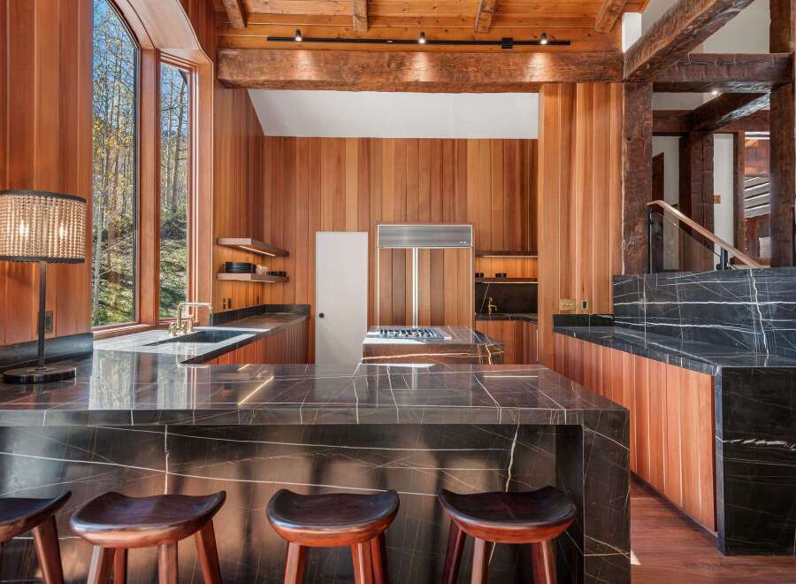 This stunning kitchen boasts a large island with dark marble countertops and wooden stools, perfect for casual dining.