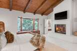 This stunning bedroom boasts a cozy fireplace, a large bay window overlooking a snowy landscape, and a wood-beamed ceiling.