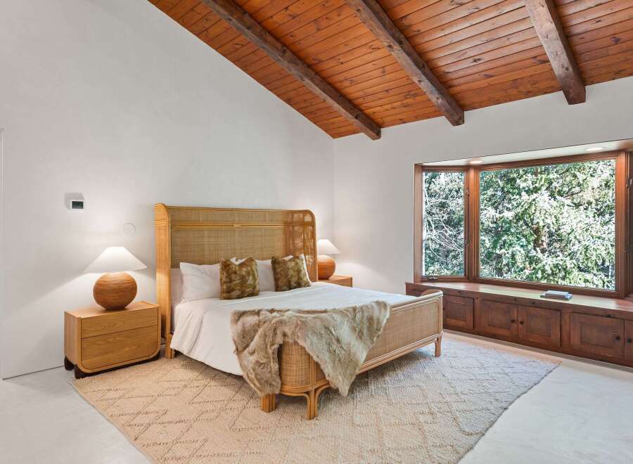 This bedroom boasts a stunning wooden beam ceiling and large bay window overlooking a lush green landscape.