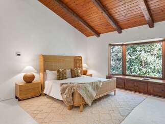 This bedroom boasts a stunning wooden beam ceiling and large bay window overlooking a lush green landscape.