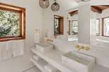 This luxurious bathroom boasts a stunning double vanity with marble sinks and gold fixtures, complemented by large windows offering breathtaking views of the surrounding trees.