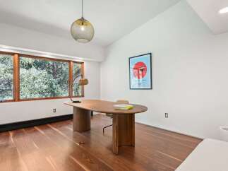 This modern home office boasts a stunning walnut wood floor, large windows offering abundant natural light, and a sleek, mid-century modern desk.