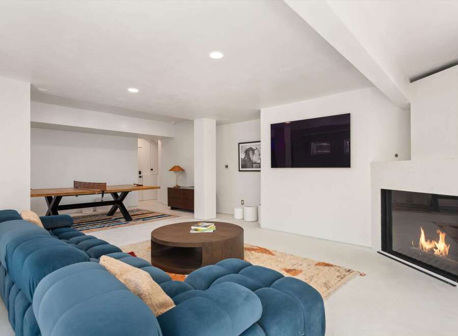 This stunning modern home boasts a spacious game room with a ping pong table, plush sectional sofa, and a cozy fireplace.