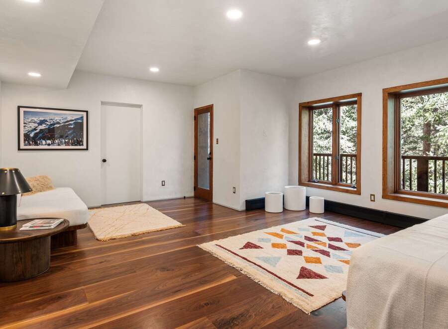 This stunning bedroom boasts large windows offering breathtaking views of the surrounding landscape, complemented by hardwood floors and stylish rugs.