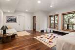 This stunning bedroom boasts large windows offering breathtaking views of the surrounding landscape, complemented by hardwood floors and stylish rugs.