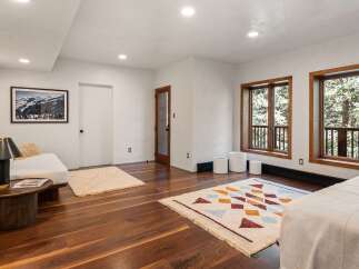 This stunning bedroom boasts large windows offering breathtaking views of the surrounding landscape, complemented by hardwood floors and stylish rugs.