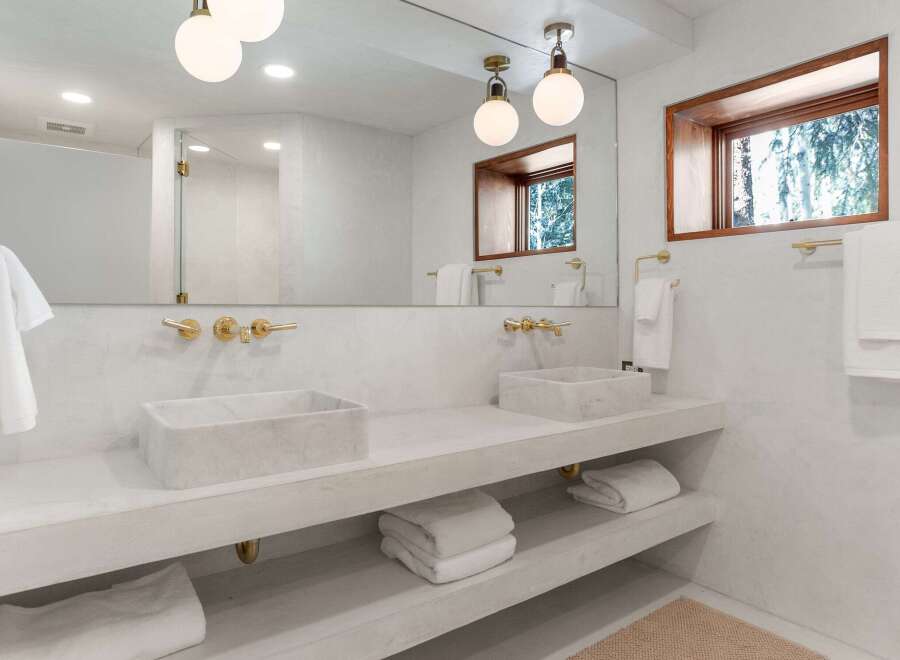 This stunning bathroom boasts a double vanity with marble sinks, sleek gold fixtures, and built-in shelving for added convenience.