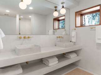 This stunning bathroom boasts a double vanity with marble sinks, sleek gold fixtures, and built-in shelving for added convenience.