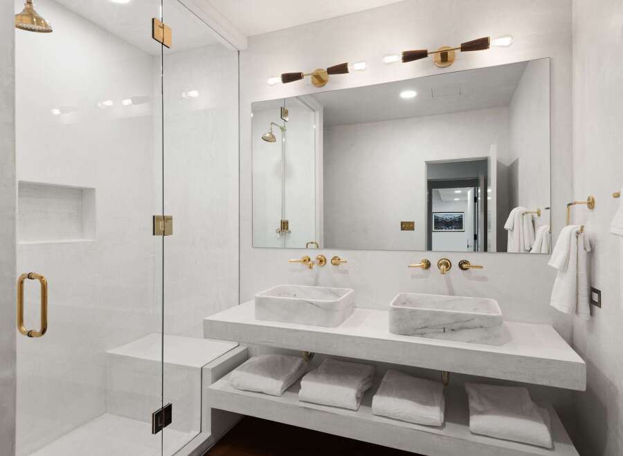 This luxurious bathroom boasts a double vanity with marble sinks and gold fixtures, complemented by a spacious glass-enclosed shower.