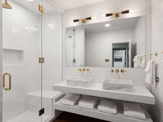 This luxurious bathroom boasts a double vanity with marble sinks and gold fixtures, complemented by a spacious glass-enclosed shower.