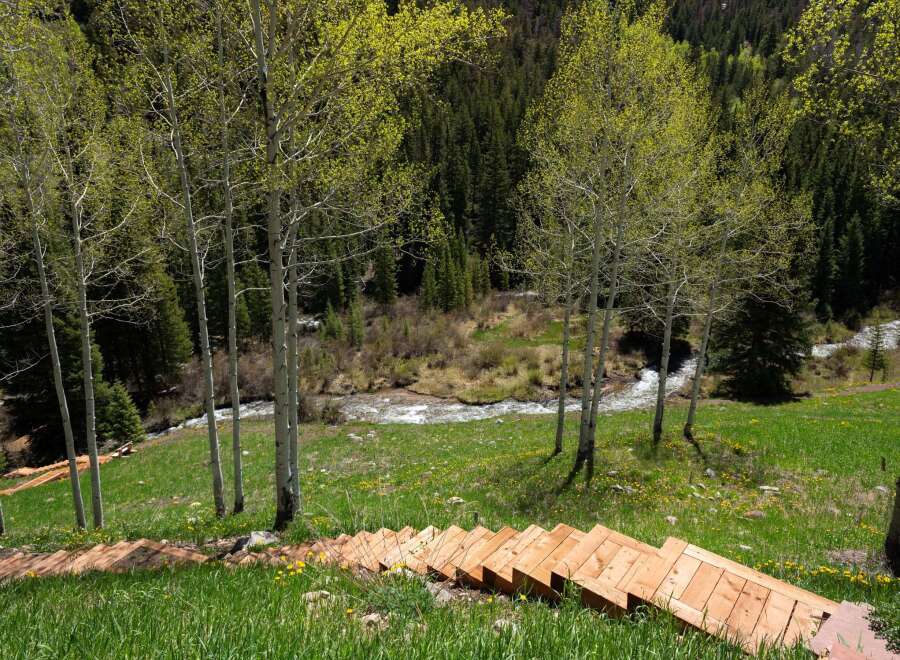 This stunning property boasts a unique wooden staircase leading down to a serene creek, nestled amidst a vibrant landscape of wildflowers and aspen trees.