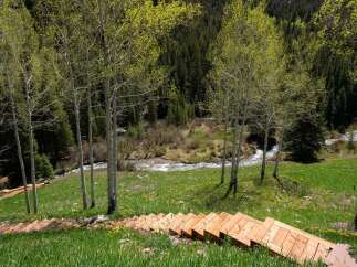 This stunning property boasts a unique wooden staircase leading down to a serene creek, nestled amidst a vibrant landscape of wildflowers and aspen trees.