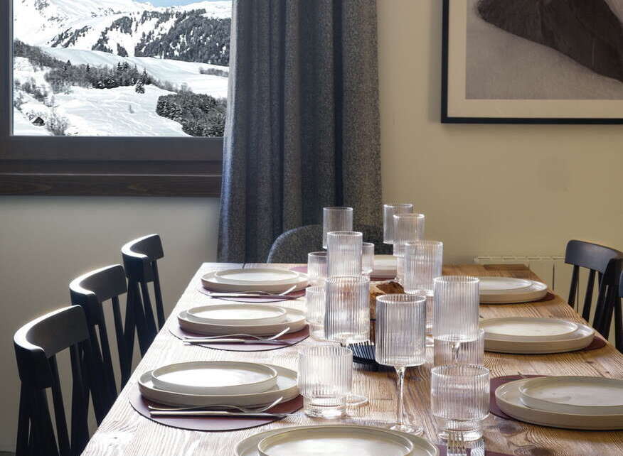 This stunning chalet boasts a large dining table perfect for family gatherings, complete with modern tableware and a breathtaking view of the snowy mountains.
