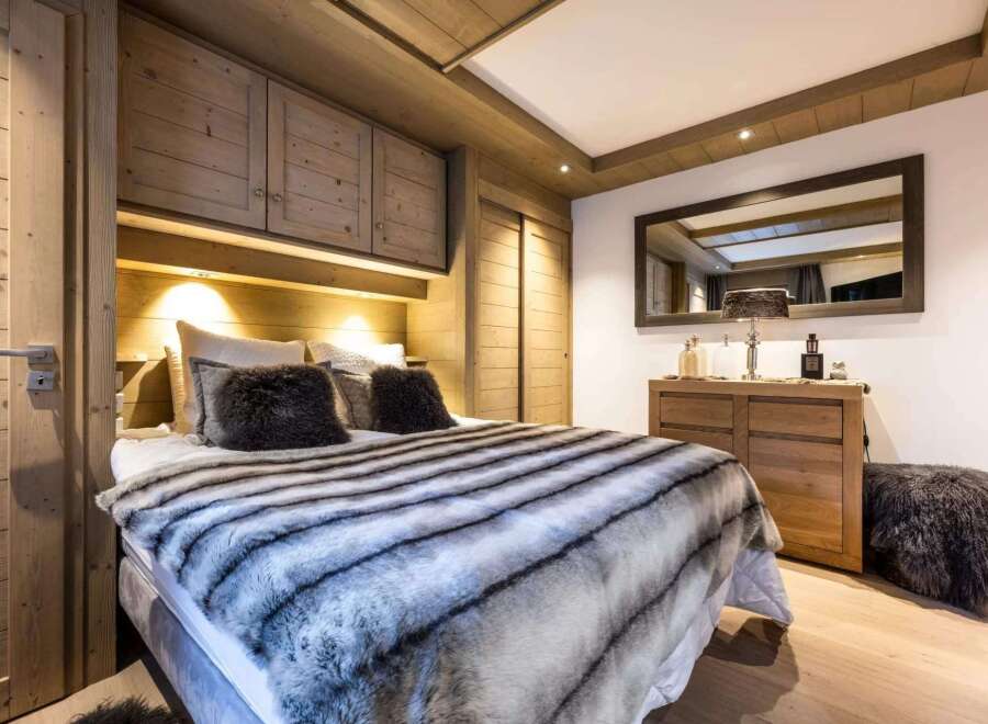 Cozy chalet bedroom with built-in wooden wardrobes and a plush fur throw on the bed.