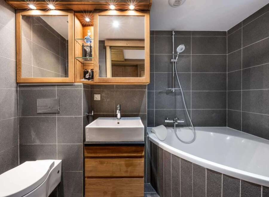 Modern bathroom with a corner bathtub, stylish wooden vanity, and sleek gray tile.