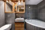 Modern bathroom with a corner bathtub, stylish wooden vanity, and sleek gray tile.