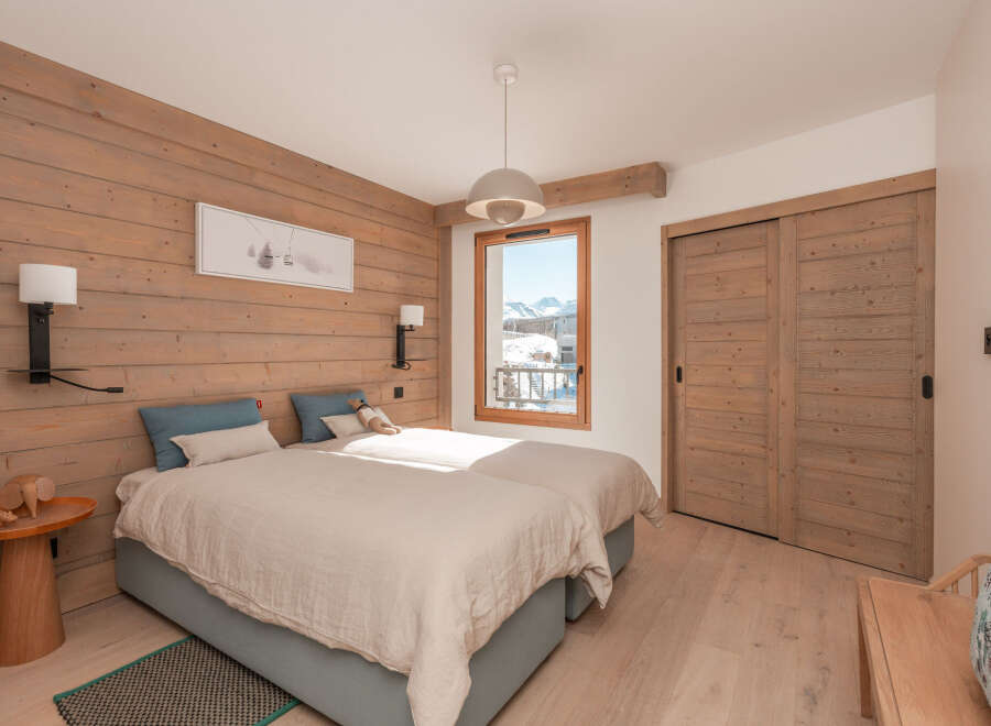 Cozy twin bedroom with wood-paneled walls and a view of the snowy mountains.