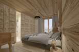 This stunning bedroom boasts a cozy and modern design, featuring a plush gray bed, wooden walls and ceiling, and large windows offering breathtaking views.