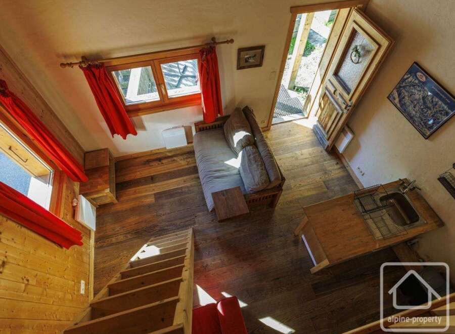 This charming chalet boasts a cozy open-plan living area with a comfortable sofa and a rustic wooden kitchenette.
