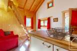 Cozy chalet apartment with wooden interior, featuring a red sofa, a wooden staircase leading to a loft, and a small kitchen with wooden countertops.