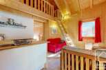 Cozy chalet apartment featuring a well-equipped kitchenette, a comfortable red sofa, and a charming wooden loft bedroom accessible by a ladder.