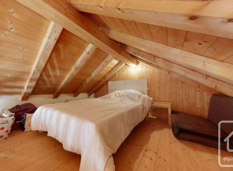 Cosy attic bedroom with wooden beams and floors, featuring a comfortable double bed and a fold-out chair for extra seating.