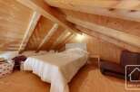 Cosy attic bedroom with wooden beams and floors, featuring a comfortable double bed and a fold-out chair for extra seating.
