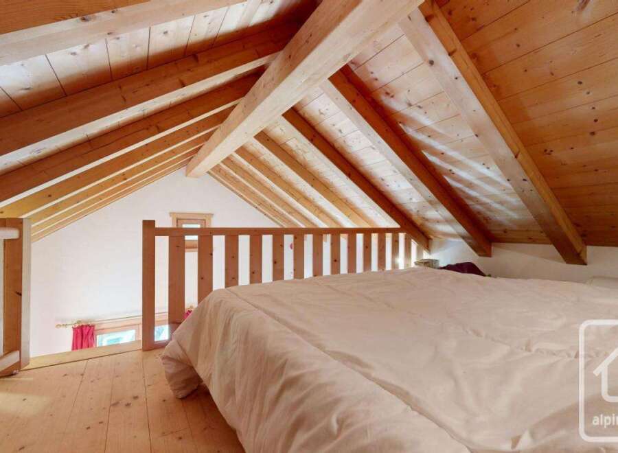 Cosy attic bedroom with wooden beams and a mezzanine level, offering a unique and charming atmosphere.