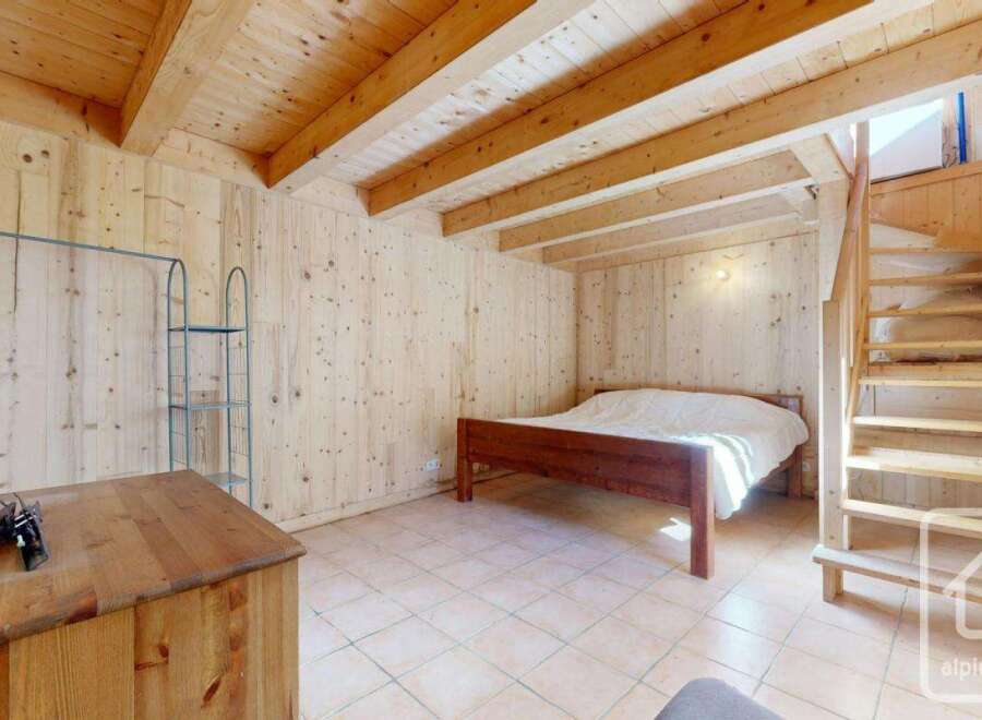 This charming wooden chalet bedroom features a double bed, built-in wooden shelving, and a wooden staircase leading to an upper level.