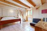 Cozy chalet bedroom with wooden walls and ceiling, featuring a double bed, a small sofa, and a wooden staircase leading to an upper level.