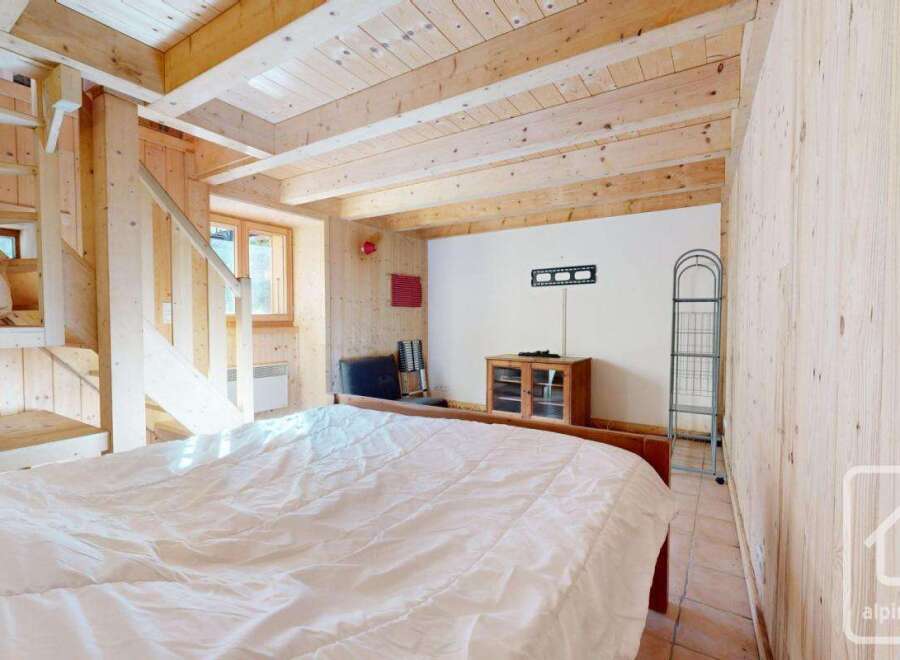 Cosy chalet bedroom with wooden walls and ceiling, featuring a double bed and built-in bunk beds.