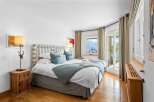 This luxurious bedroom boasts stunning lake views from its large windows and patio doors.