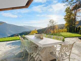 Luxury mountain retreat with expansive patio featuring a large stone table and ornate chairs, perfect for al fresco dining while enjoying breathtaking views.