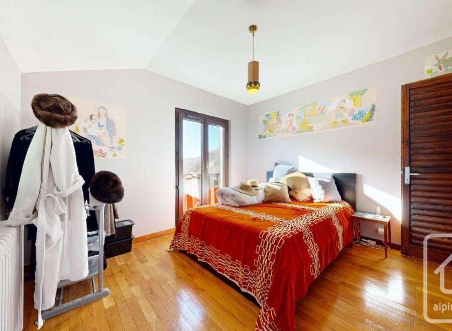 Charming bedroom with wooden floors, a large window offering mountain views, and a cozy bed with an orange blanket.
