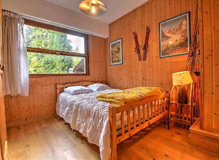 Cozy wooden bedroom with a double bed, large window overlooking trees, and vintage ski decor.