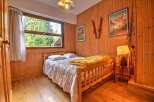 Cozy wooden bedroom with a double bed, large window overlooking trees, and vintage ski decor.