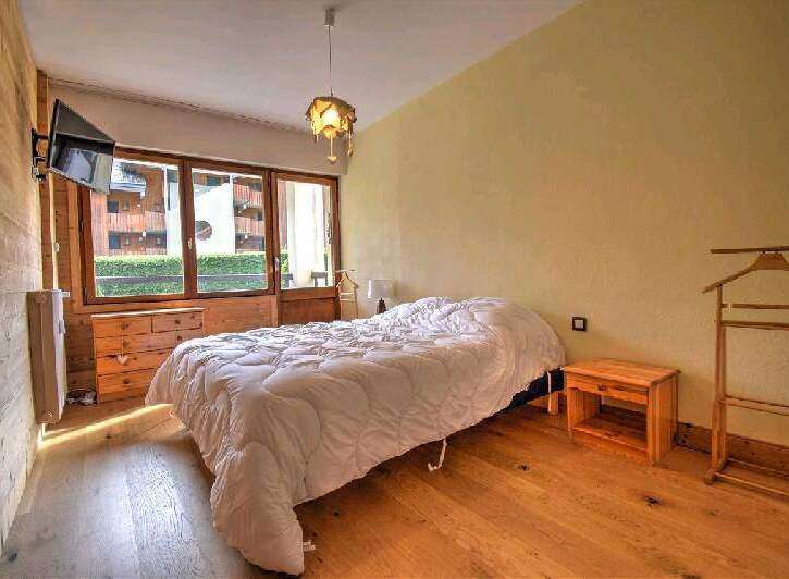Cozy bedroom with wooden floors and walls, featuring a comfortable double bed and large windows offering scenic views.